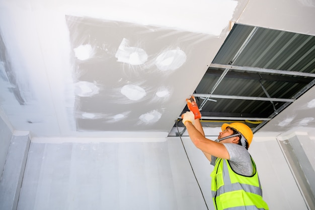 travailleurs de la construction portant des uniformes Installez un plafond de gypse à l'intérieur de la maison et du bâtiment. Utilisez un tournevis électrique pour installer le plafond.