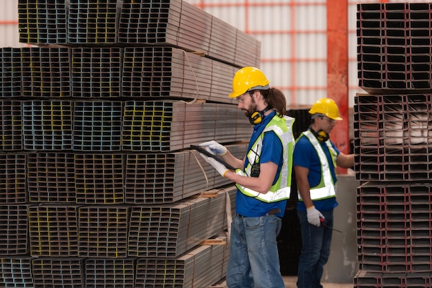 Les travailleurs de l'entrepôt en casque et casque se tiennent dans l'entrepôt pour compter et inspecter l'acier