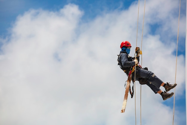 Les travailleurs masculins contrôlent la corde d'oscillation vers le bas la hauteur de l'accès à la corde du réservoir l'inspection de l'épaisseur de la plaque de la coque du réservoir de gaz fond bleu ciel.