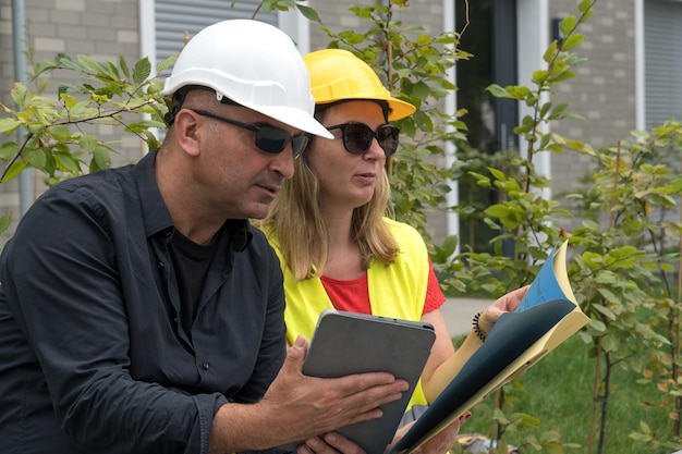 Photo des travailleurs portant un gilet de sécurité et un casque vérifient le plan de travail et les papiers sur une tablette numérique.