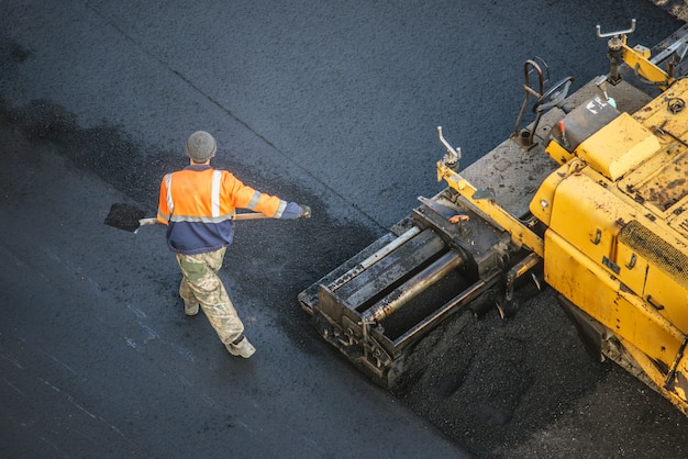 Les travailleurs posent un nouveau revêtement d'asphalte en utilisant du bitume chaud. Travaux de machinerie lourde et de finisseur. Vue de dessus
