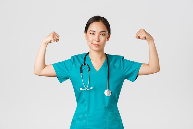 , les travailleurs de la santé et la prévention du concept de virus. Femme médecin asiatique professionnelle confiante, infirmière en gommage souriant impertinent et flex biceps, étant des muscles forts, show-off