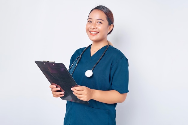 Travailleurs de la santé souriant jeune infirmière asiatique portant un uniforme bleu avec un stéthoscope écrivant sur un presse-papiers pendant les examens quotidiens isolés sur fond blanc Concept de médecine de soins de santé