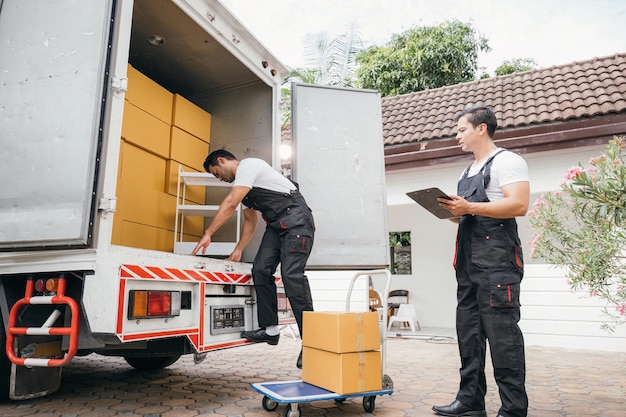 Les travailleurs en uniforme de la compagnie de déménagement déchargent des boîtes et des meubles du camion, faisant preuve d'un excellent travail d'équipe. Leur dévouement garantit un déménagement en douceur dans la nouvelle maison, assurant le bonheur du jour du déménagement.