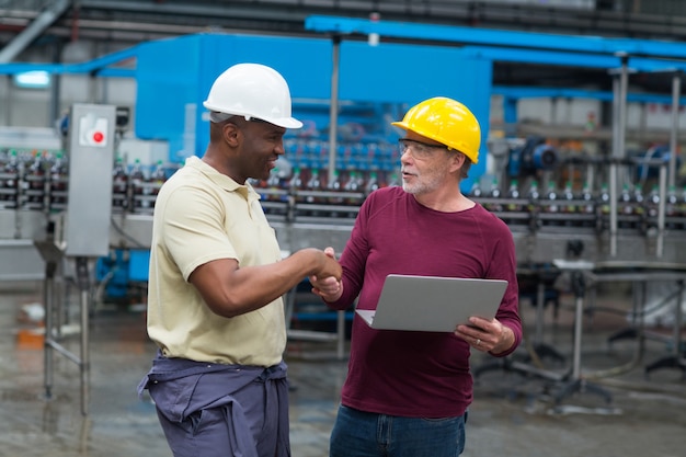 Travailleurs d'usine avec ordinateur portable se serrant la main avec son collègue