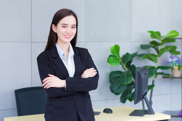 Travailleuse asiatique professionnelle qui a pendant qu'elle croise le bras et sourit sur le mur du bureau