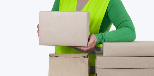 Travailleuse dans un gilet vert debout près de beaucoup de boîtes en papier avec commande vierge, concept de livraison.