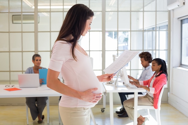 Une travailleuse enceinte touche le ventre et regarde le dossier