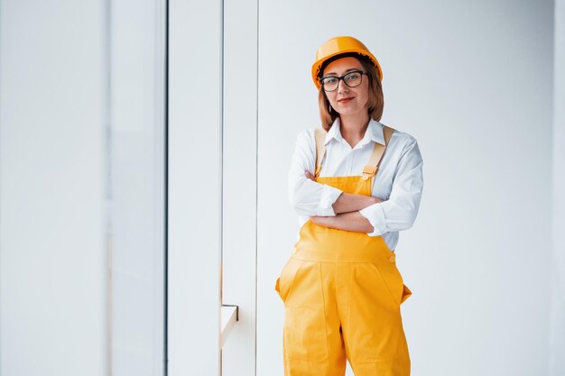 Travailleuse ou ingénieure en uniforme jaune et casque debout à l'intérieur