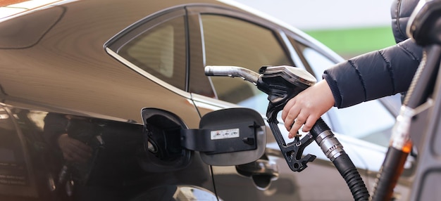 Travailleuse main tenant l'huile de remplissage de carburant de la buse dans le réservoir de la voiture à une station-service à pompe pour le concept