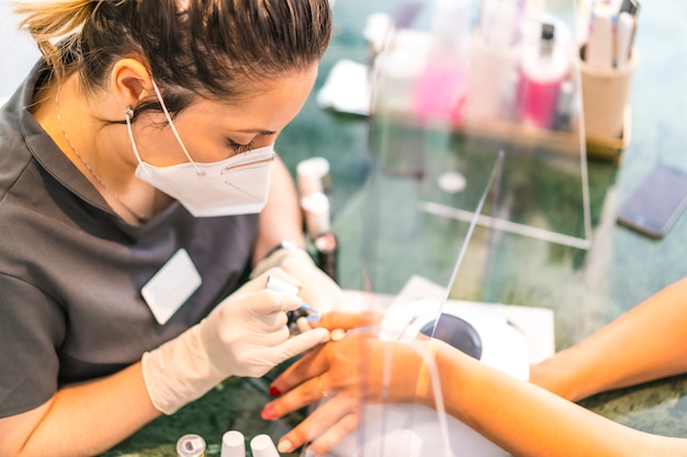 travailleuse avec masque facial peignant des ongles colorés du client. Réouverture après la pandémie de corod-19. Salon de manucure et pédicure. Coronavirus