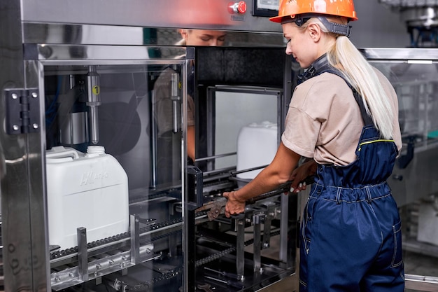 Travailleuse en usine préparant la ligne robotique pour l'embouteillage et l'emballage des bouteilles