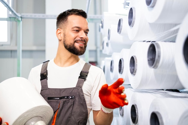 Photo travailleuse d'une usine textile changeant la bobine de fil sur une machine à tricoter industrielle