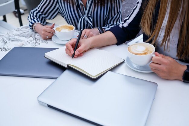 Des travailleuses souriantes et prospères travaillent ensemble, travaillent sur un ordinateur portable sur la terrasse, des collègues féminines sont occupées à discuter d'idées, des filles dans un café lors d'une réunion d'affaires. Concept d'entreprise