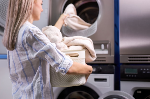 Travaux ménagers: femme chargeant des vêtements dans une machine à laver. dame caucasienne aime le processus de nettoyage. se concentrer sur les serviettes dans le panier