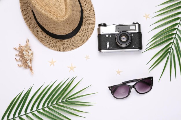 Travel flat lay Hat avec lunettes de soleil étoiles de mer coquillages et feuilles de palmier appareil photo sur fond blanc Vue de dessus