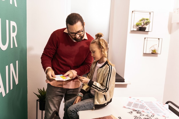 Être attentif. Jolie fille blonde avec une coiffure inhabituelle à la recherche attentive tout en ayant une leçon avec son professeur