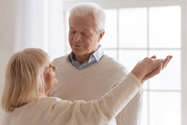 Être ensemble. Bel homme âgé en regardant sa femme et souriant tout en dansant avec elle