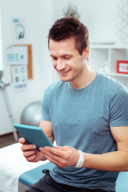 Être en ligne. Bel homme positif regardant l'écran de la tablette tout en surfant sur Internet