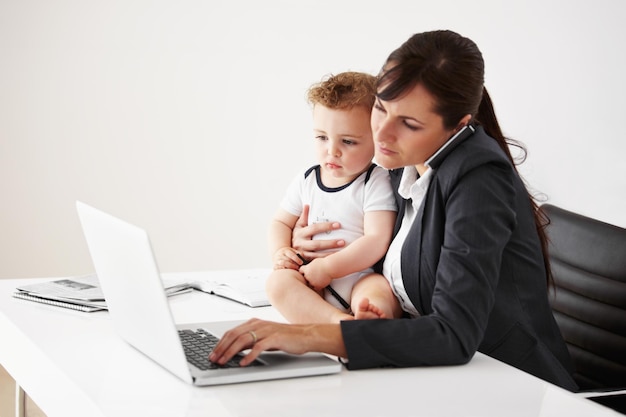 Être une mère qui travaille est un exercice d'équilibre Une mère qui travaille parle au téléphone tout en tenant un bébé et en tapant sur son ordinateur portable