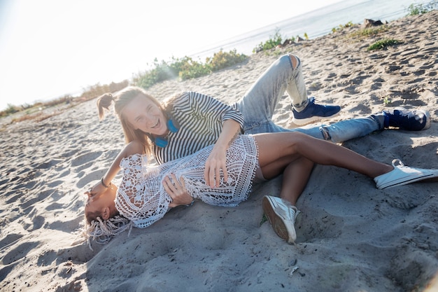 Étreindre petite amie. Bel homme portant un jean et une chemise rayée serrant sa petite amie allongée sur le sable
