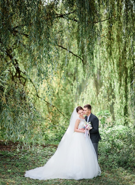 Étreintes douces de couple de mariage posant sous les arbres verts à l&#39;extérieur