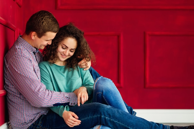 Étreintes sensuelles d'un couple assis sur le sol près du mur rouge