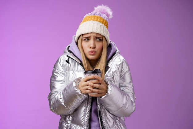 Tremblement inconfortable mignonne moue jeune fille blonde se sentir glaciale hiver neigeux à l'extérieur secouant basse température tenir à emporter tasse de café chaud réchauffant, fond violet