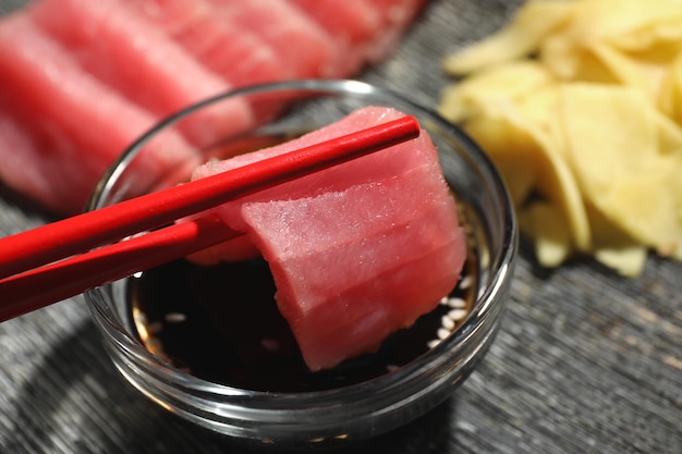 Tremper un savoureux morceau de sashimi de thon cru frais dans de la sauce soja au gros plan du tableau noir