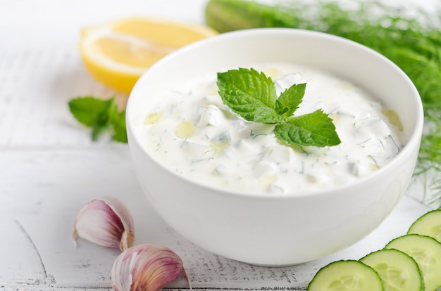 Trempette grecque ou vinaigrette tzatziki et ingrédients décorés à l’huile d’olive et à la menthe sur une table en bois blanche