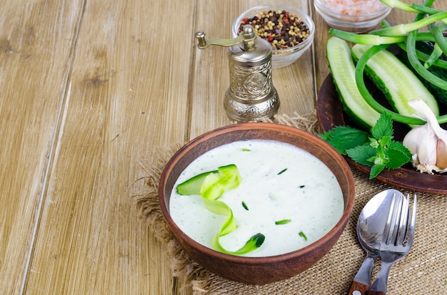 Trempette traditionnelle grecque ou vinaigrette tzatziki préparée avec du concombre râpé, du yaourt, de l'huile d'olive et de l'aneth frais sur une table en bois dans un bol en céramique.