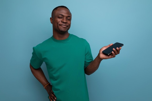 Trente ans beau agréable avec la peau foncée homme américain vêtu d'un t-shirt de base tient un smartphone avec sa main et sourit