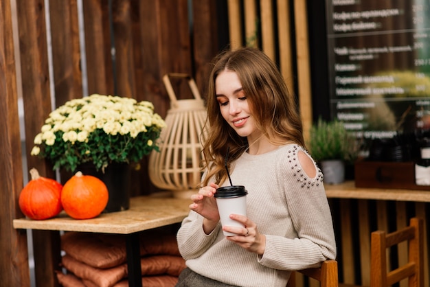 Très belle jeune femme, asseyez-vous dans un café et buvez du café ou du thé avec un croissant, vue de face de la rue