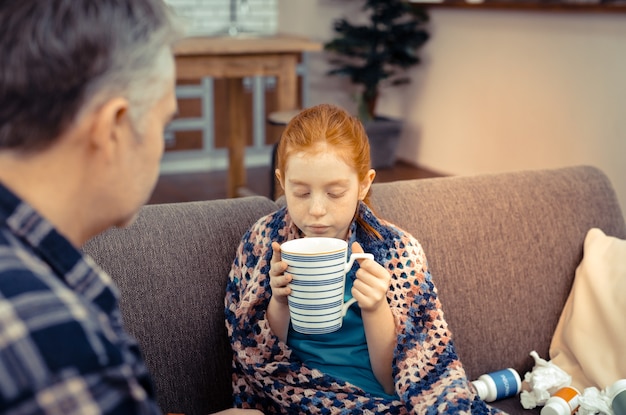 Très chaud. Jolie fille mignonne soufflant dans le thé tout en tenant une tasse dans ses mains