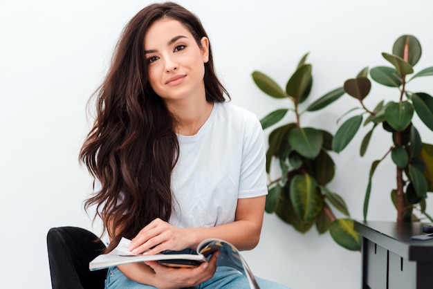 Très jolie brune aux cheveux longs tient un magazine dans ses mains.