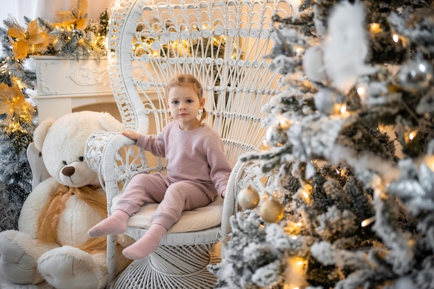 Très jolie petite fille charmante blonde en pyjama près des sapins de Noël dans un intérieur lumineux de la maison