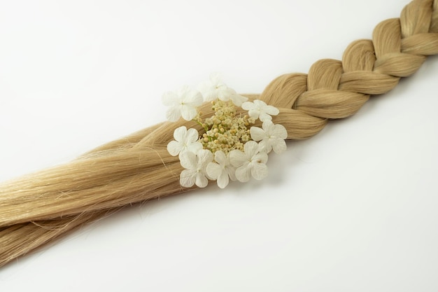 Une tresse de cheveux blonds avec une fleur blanche dessus allongé sur un fond blanc