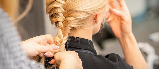 Tresse de tressage. Mains de coiffeuse tresse longue tresse pour une femme blonde dans un salon de coiffure.