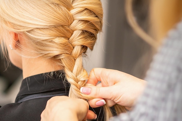 Tresse de tressage. Mains de coiffeuse tresse longue tresse pour une femme blonde dans un salon de coiffure.