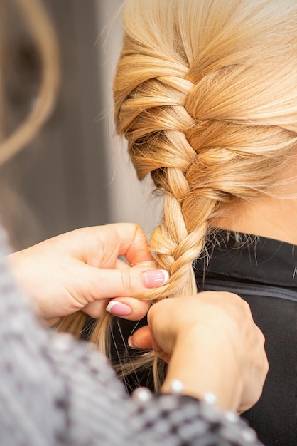 Tresse de tressage. Mains de coiffeuse tresse longue tresse pour une femme blonde dans un salon de coiffure.