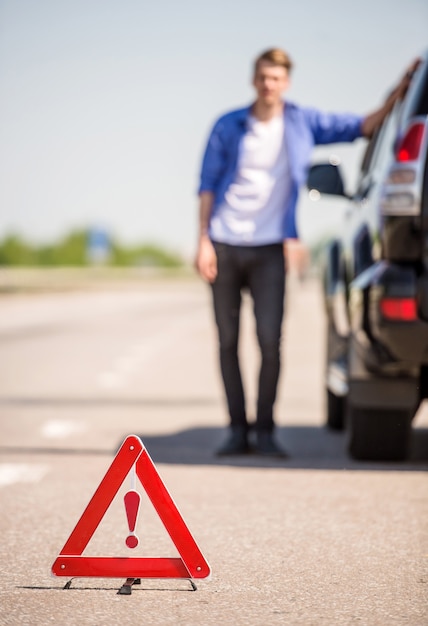 Triangle de signalisation rouge avec une voiture en panne sur la route.