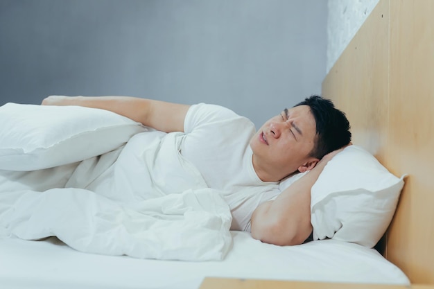 Triste asiatique allongé dans un lit sous une couverture un homme déprimé le matin