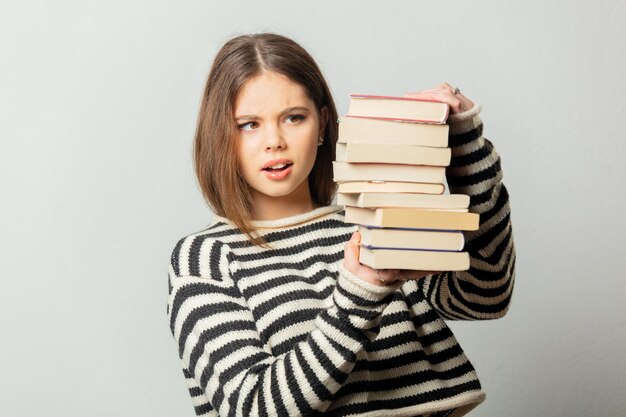 Triste belle fille en pull rayé avec des livres sur fond blanc