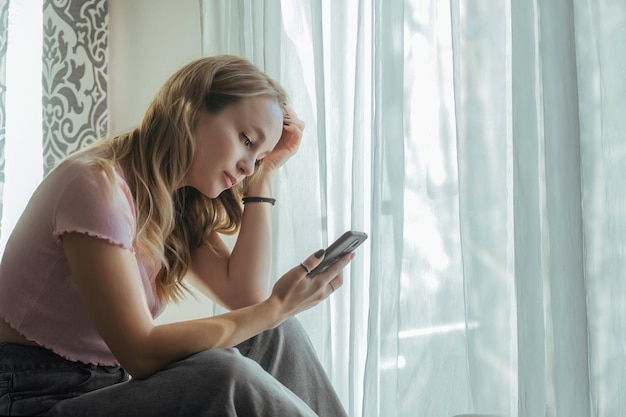 Triste belle fille regardant le téléphone à la maison