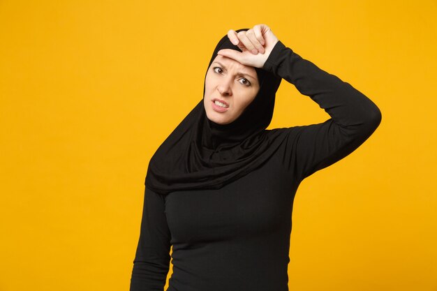 Triste bouleversée pleurant confuse jeune femme musulmane arabe en vêtements noirs hijab posant isolé sur mur jaune, portrait. Concept de mode de vie de l'Islam religieux.