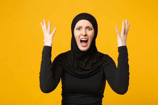 Triste bouleversée pleurant confuse jeune femme musulmane arabe en vêtements noirs hijab posant isolé sur mur jaune, portrait. Concept de mode de vie de l'Islam religieux.