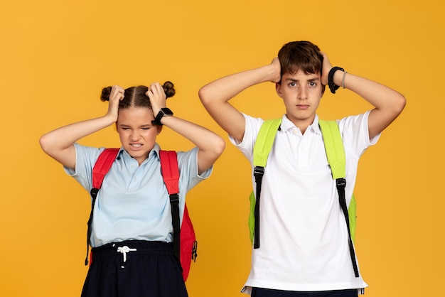 Triste en colère fatigué adolescent européen garçon et fille avec des sacs à dos couvrent les oreilles avec les mains