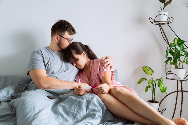 Triste couple au lit regardant un test de grossesse négatif
