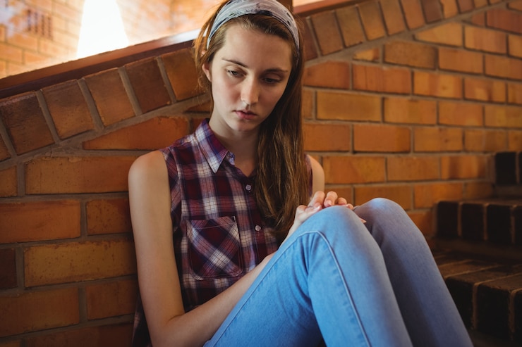 Photo triste écolière assise seule sur l'escalier