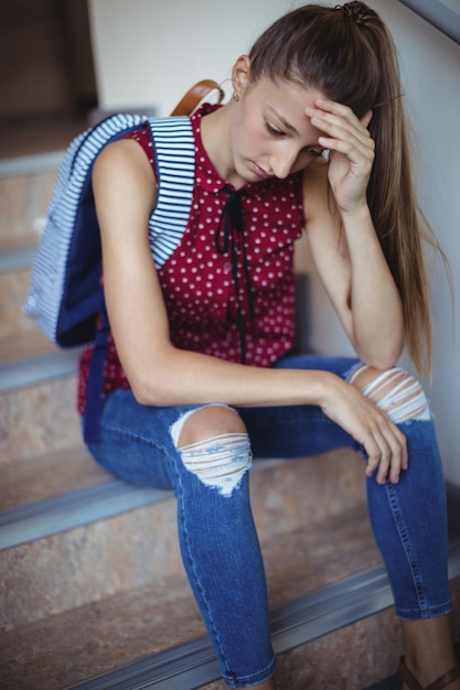 Photo triste écolière assise seule sur l'escalier